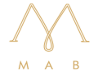 Il logo presenta due linee dorate che formano un motivo a "M" stilizzata, con una goccia centrale sospesa al vertice inferiore, conferendo un aspetto elegante e distintivo. Sotto il motivo è riportata la scritta "MAB" in lettere maiuscole, anch'essa in oro.